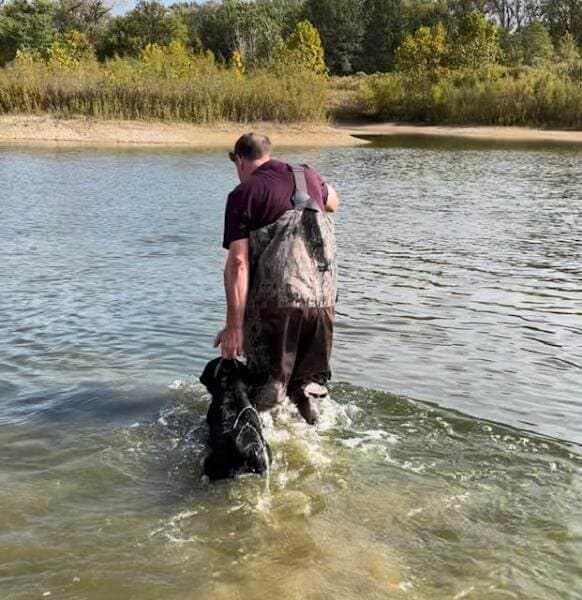 A man standing in water with a dog.