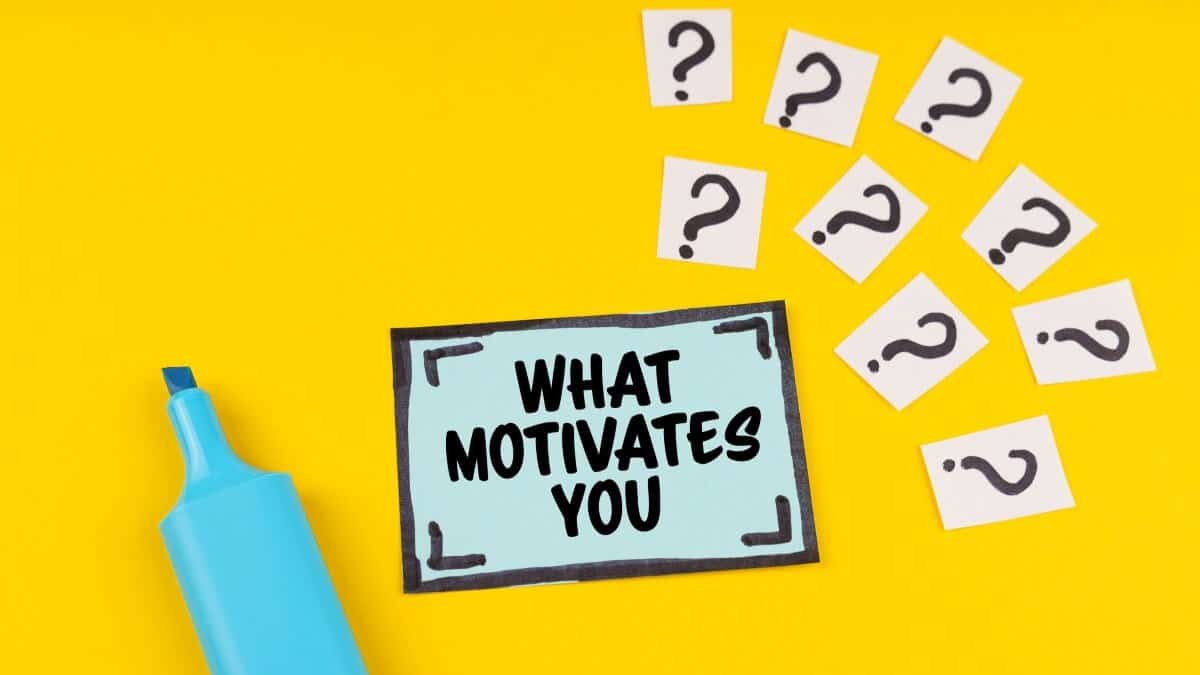 On the yellow surface is a marker, question marks and a sticker with the inscription - WHAT MOTIVATES YOU.