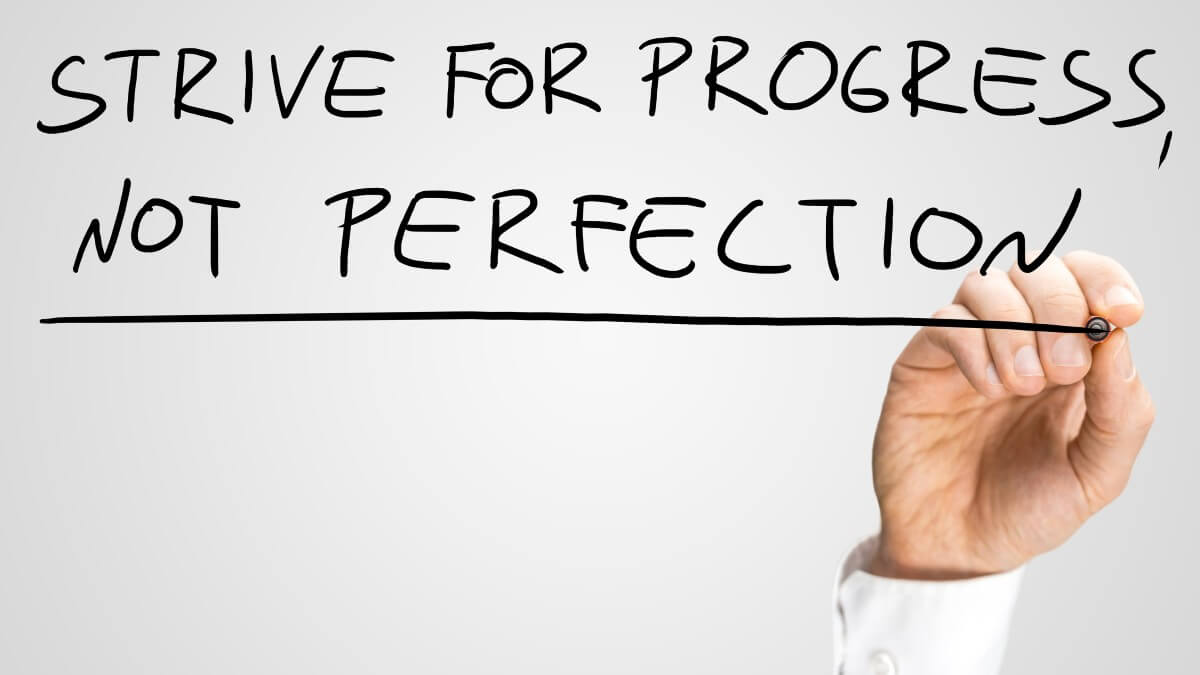 Man writing the idiom - Strive For Progress Not Perfection - on a virtual interface with a black marker pen over grey with copyspace in a motivational business message.
