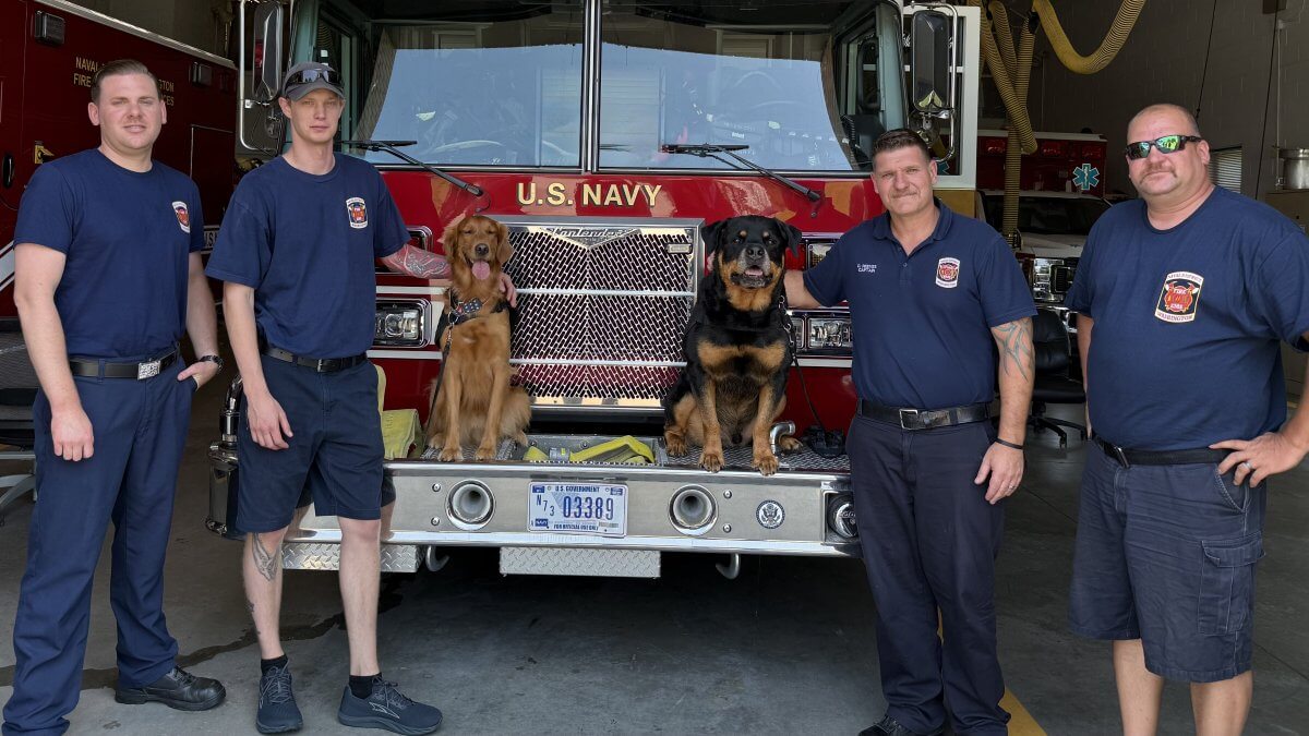 Five firefighters pose with their dogs in front of a fire truck.