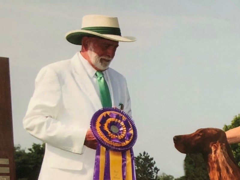 Sam Houston McDonald, dressed in white suit with a hat, presenting a ribbon to a dog