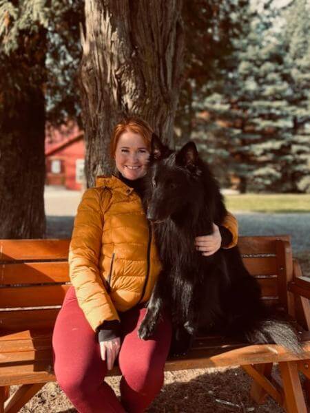 A girl and a black dog sitting on the bench.