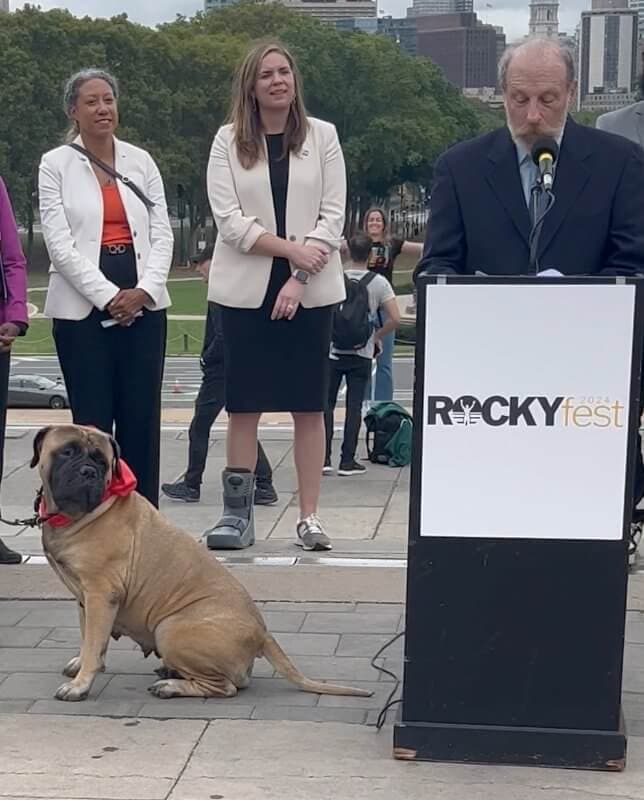 ROCKYFEST 2024 LAUNCH - Steve Griffith, Kennel Club of Philadelphia Director of Communications, details The National Dog Show’s involvement in RockyFest 2024 during the October press conference announcing RockyFest 2024 activities centering on the iconic movie, Rocky. Representing Rocky’s companion and training partner, Butkus, and the Bullmastiff breed is Wasabi, a member of the National Dog Show Therapy Dog Ambassador Team. Created by the Philadelphia Visitor Center Corp., RockyFest is an international tourist attraction featuring bus tours, film festivals, ice skating rink date nights, and the Southpaws Yappy Hour, Thursday, Dec. 5, on the Delaware River Waterfront. Photo Credit: Kathi Graham/National Dog Show