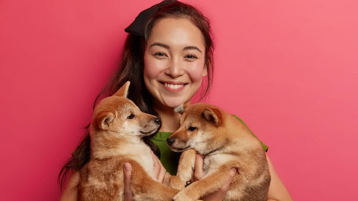 Asian woman poses with two small puppies.