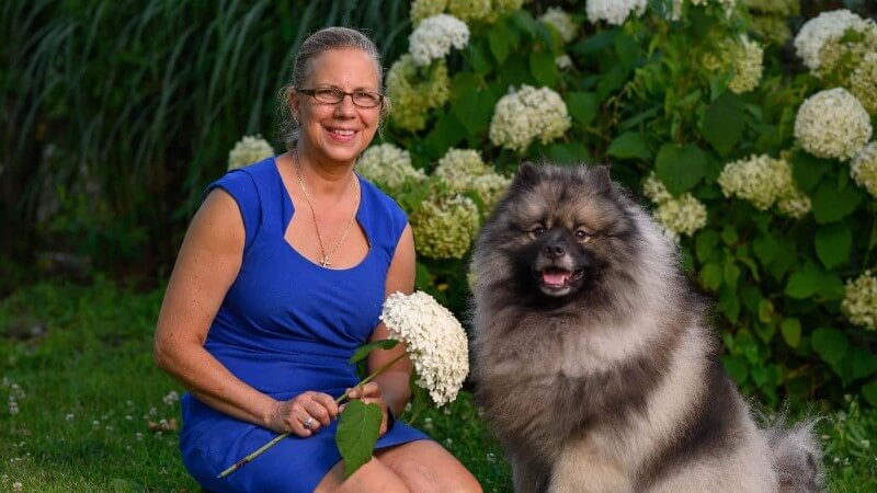 A photo of a woman posing with Keeshond dog.