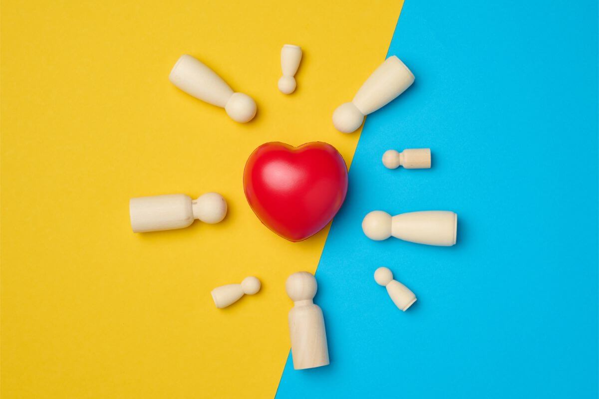 Red heart and wooden figurines of men on a yellow-blue background