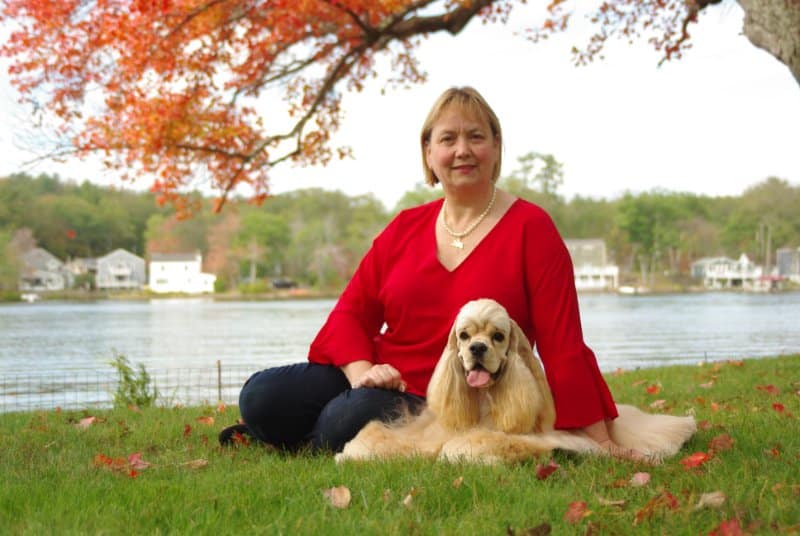 Judith Webb of SoundView Cockers, photograph of her and her Cocker Spaniel sitting on the grass near a lake