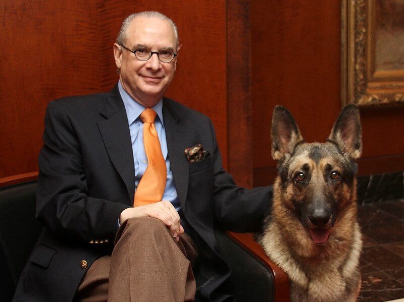 Dennis Sprung, AKC President & CEO sitting on a chair with a German Shepherd dog beside him