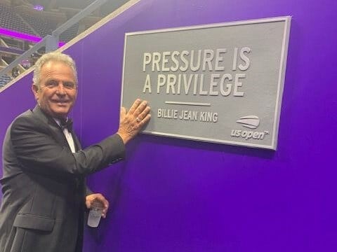 George Milutinovich, 2023 WKC Dog Show Non-Sporting Group Judge, is pictured at the show standing besides a placquette that says "Pressure is a Privilege."