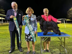 Three people standing next to a table with a black dog, at the Australian Dog Show.