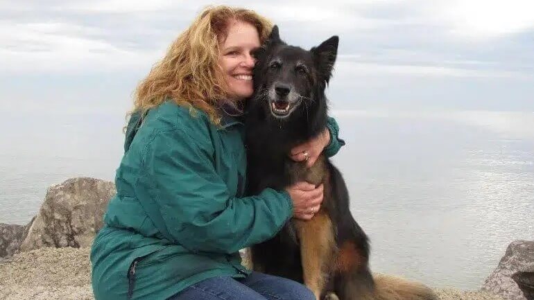 Woman sitting and hugging a purebred Belgian Tervuren dog, outdoors.