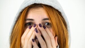 Close up portrait of scared young redhead woman wearing warm hoodie pullover.