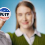 Vote, badge and hand of woman for elections, political and studio with pin on blue background.