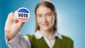 Vote, badge and hand of woman for elections, political and studio with pin on blue background.