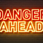 Danger ahead neon sign on brick wall background.