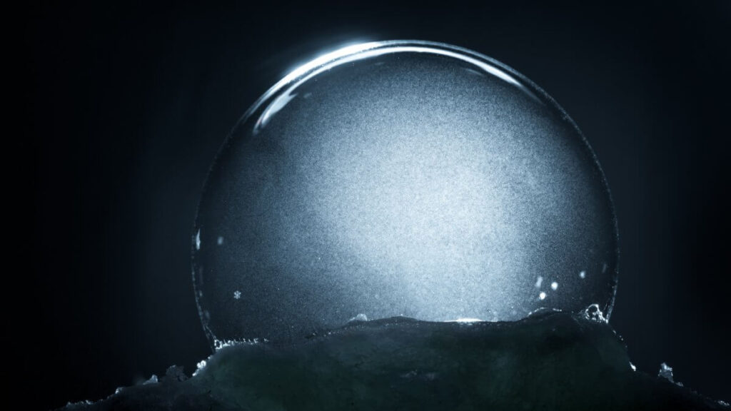 Frozen snow globe christmas magic ball with flying snowflakes. Winter Background. For Christmas and New Year Holidays precious backdrop. Ice patterns frosted on ball of soap against dark black abstract bokeh background.