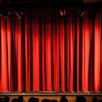A closed red stage curtain in a small theater