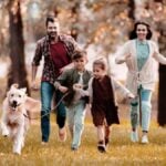 smiling family with a Labrador running on meadow in autumn-park