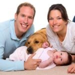 Baby, mother, and father. Happy family with Golden Retriever dog on carpet