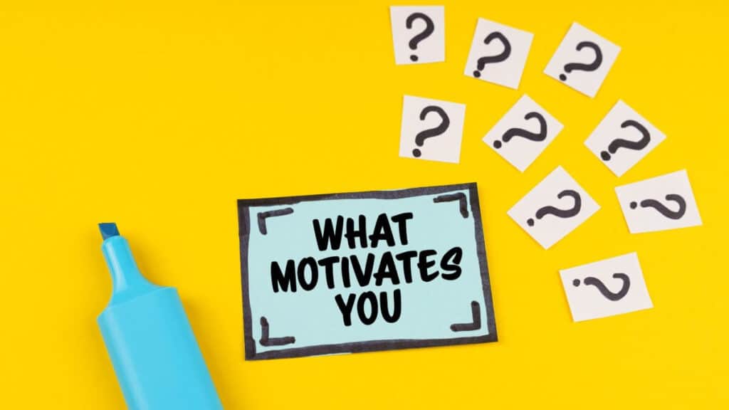 On the yellow surface is a marker, question marks and a sticker with the inscription - WHAT MOTIVATES YOU.