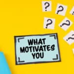 On the yellow surface is a marker, question marks and a sticker with the inscription - WHAT MOTIVATES YOU.