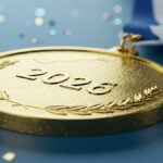 Close up of glittering 2026 championship gold medal. This macro shot captures a finely textured gold medal embossed with the year 2026 and a classic laurel wreath design.