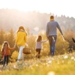 A rear view of young family with two small children and a dog on a walk in autumn nature.