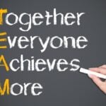 Hand of person writing together everyone achieves more on blackboard, teamwork concept.